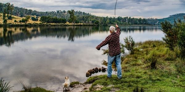 little white dog on the shore with a man who is fishing